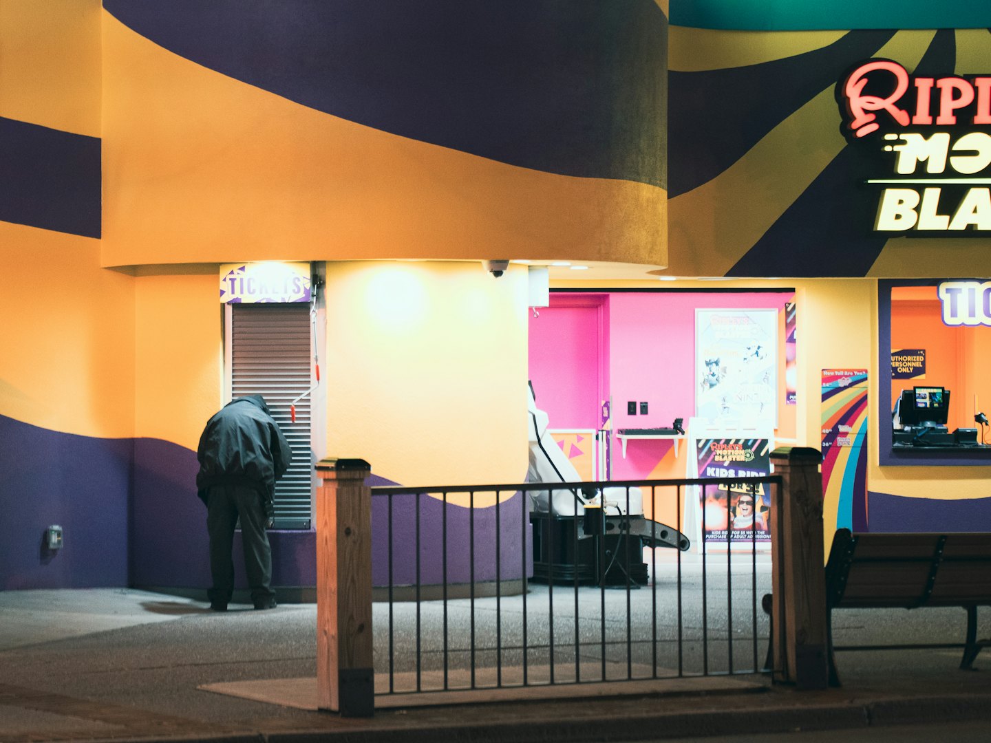 Person in a dark jacket leans over an orange striped ticket booth.